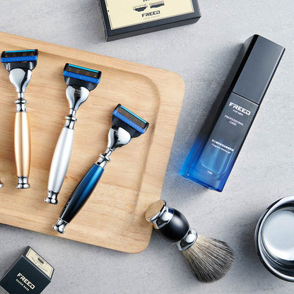 木盤上擺放三支金屬刮鬍刀，及藍色漸層瓶裝香氛露。FREED 客製化刻字