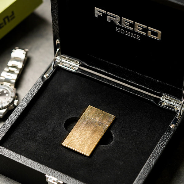 金色拉絲銅殼打火機，俯視角度，置於黑色盒內。FREED 客製化刻字。