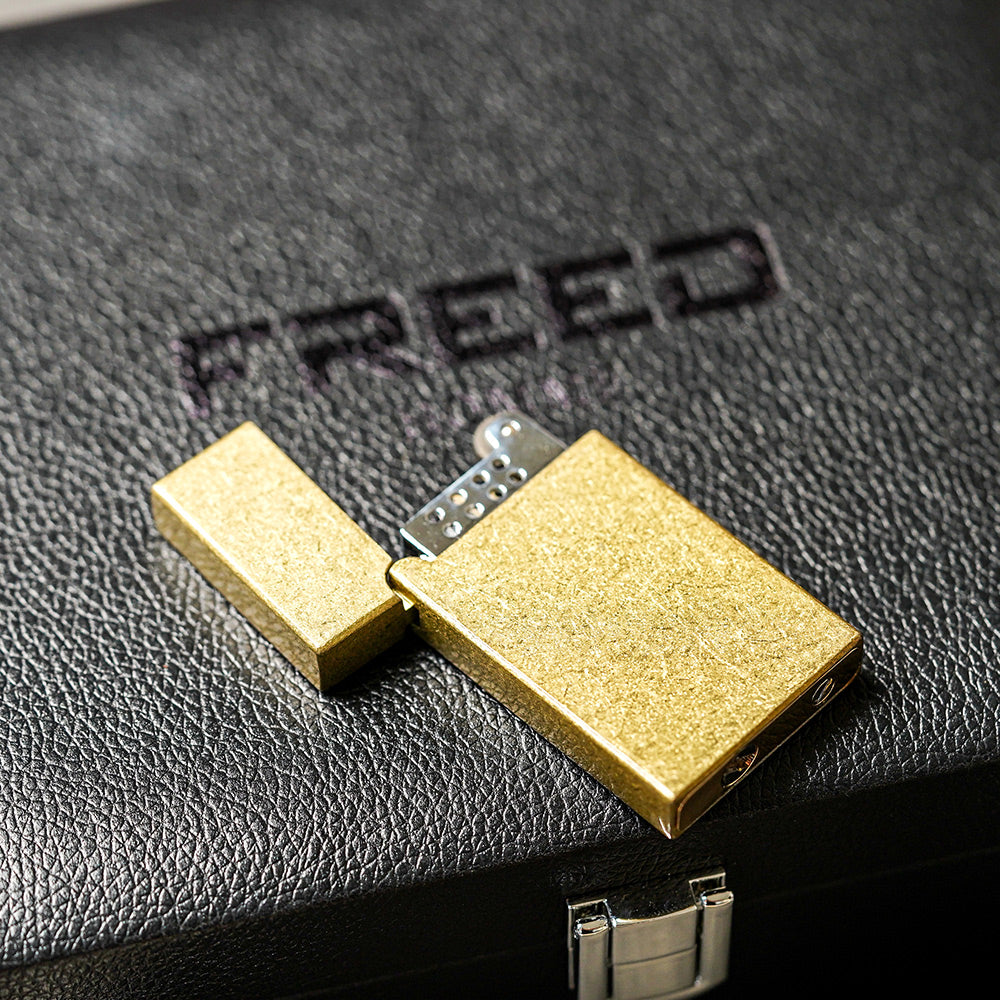金色滾花銅殼打火機，斜角展示於荔枝紋皮革盒上。FREED 客製化刻字