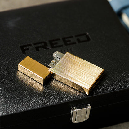 金色拉絲銅殼煤油打火機，近拍俯角，置於黑色皮盒上。FREED 客製化刻字